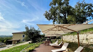 Eine Holzterrasse mit Liegestühlen und Sonnenschirmen, eine Steinmauer und Blick auf die Landschaft.