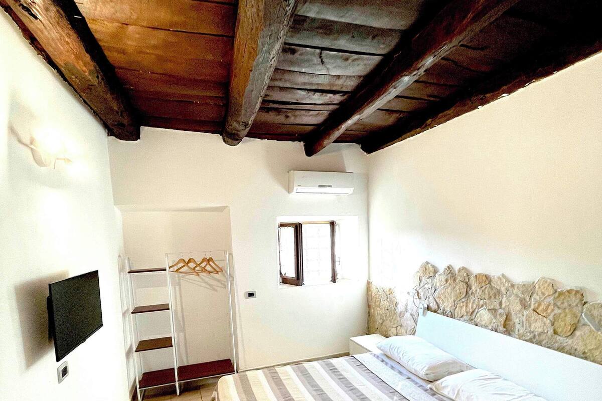 Un dormitorio con techo de madera, una cama con ropa de cama a rayas, un televisor montado en la pared y una pared de piedra.