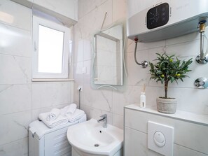 Un baño moderno con un lavamanos blanco, un espejo, una ventana, un perchero para toallas, una planta y un dispositivo con conexión Wi-Fi.