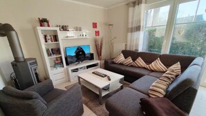 Una sala de estar con sofá, sillón, mesa de centro, televisor, estantería y chimenea.
