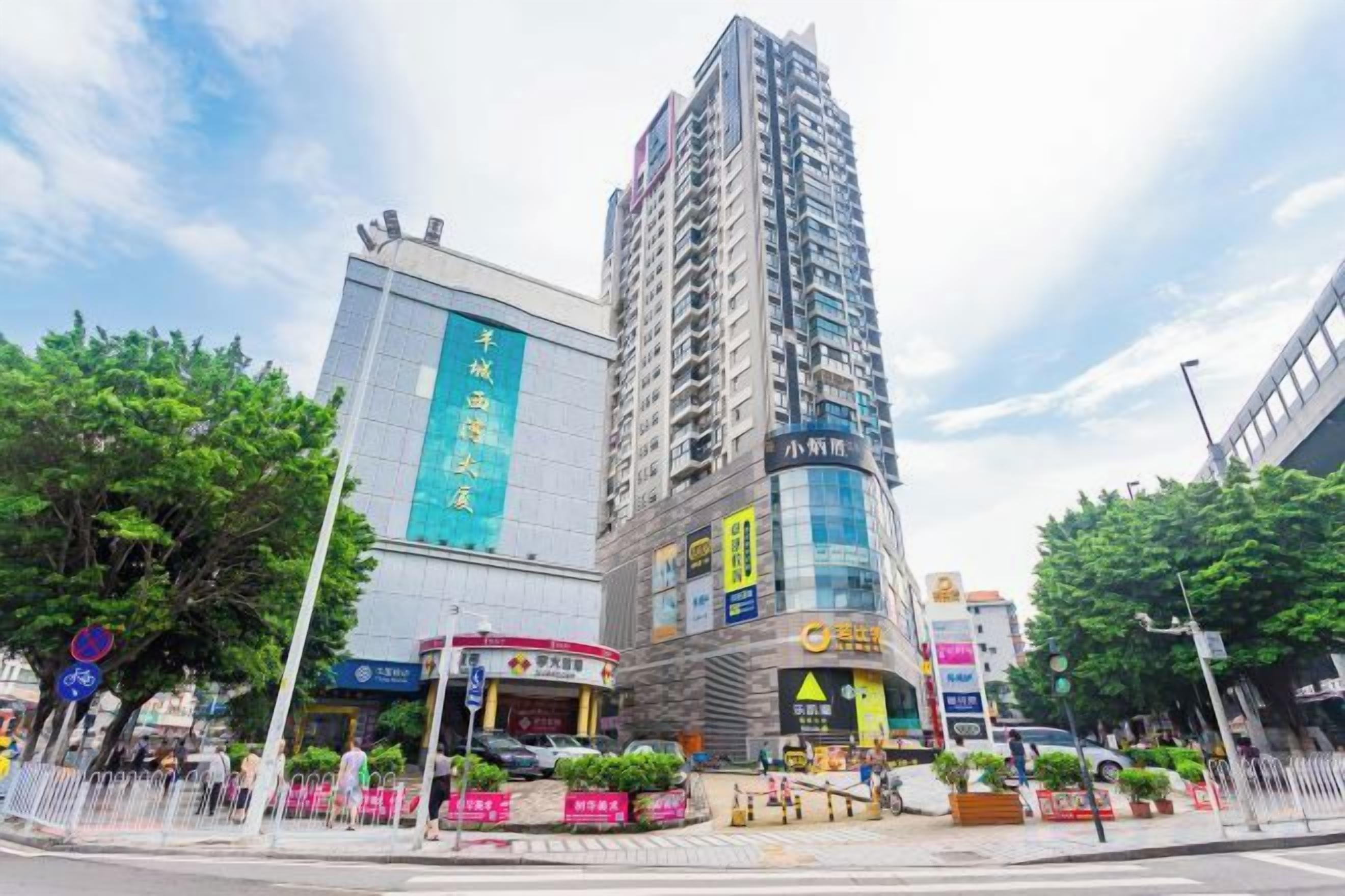 A high-rise building with a large sign, a commercial area with shops, and a pedestrian walkway.