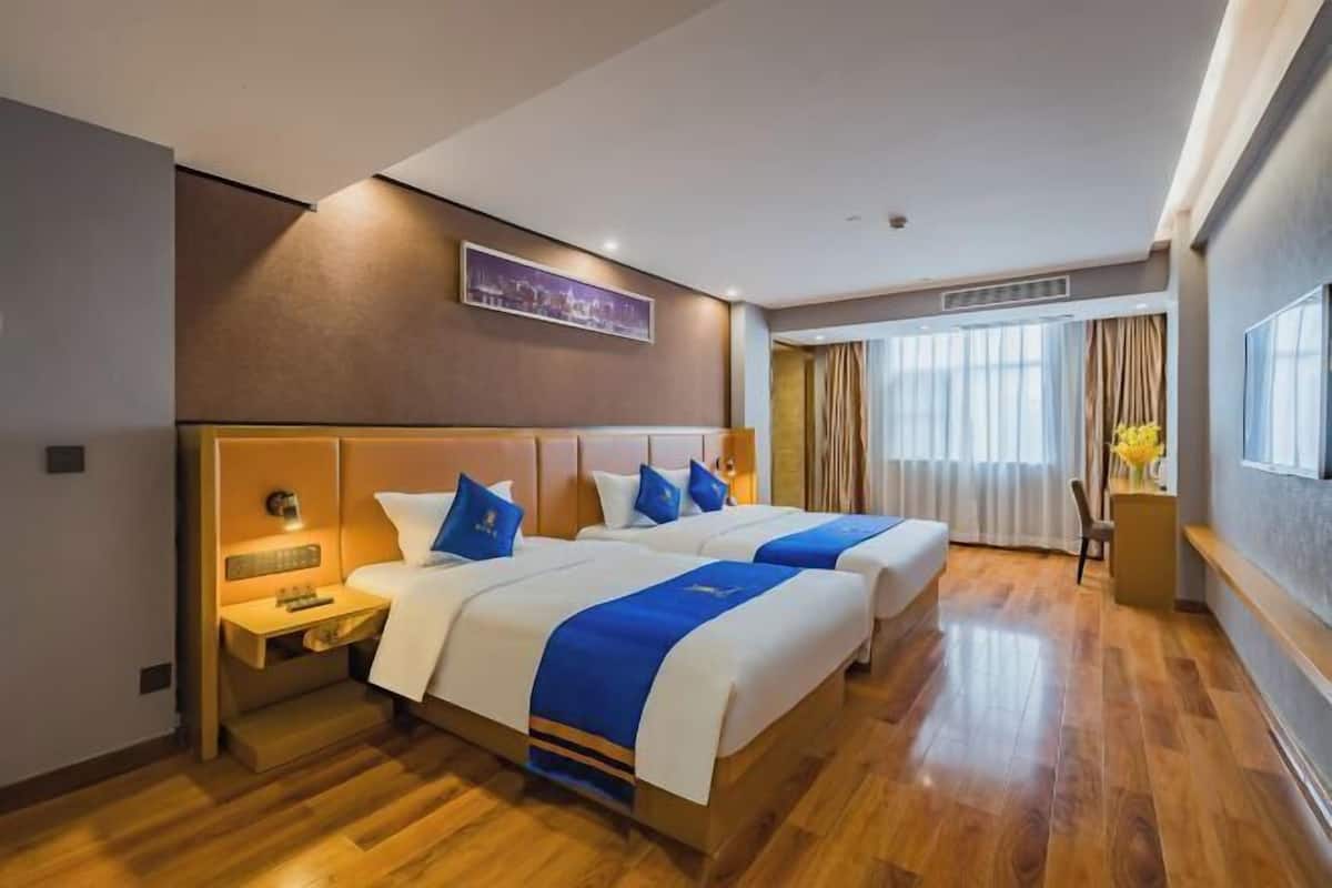A hotel room with two beds, a nightstand, a desk, and a window with curtains.