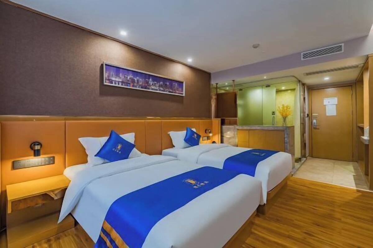 A hotel room with two beds, a cityscape painting, a minibar, and a wooden floor.