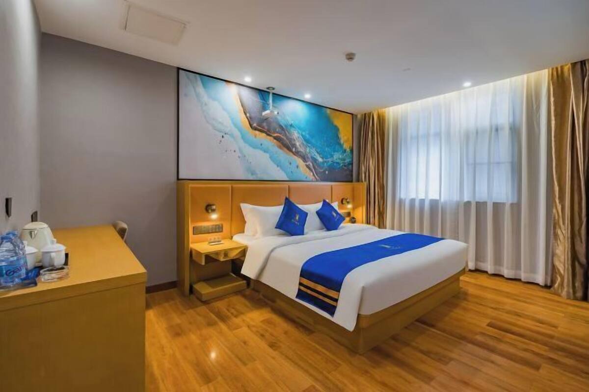 A hotel room with a bed, a desk, a nightstand, and a large abstract painting on the wall.