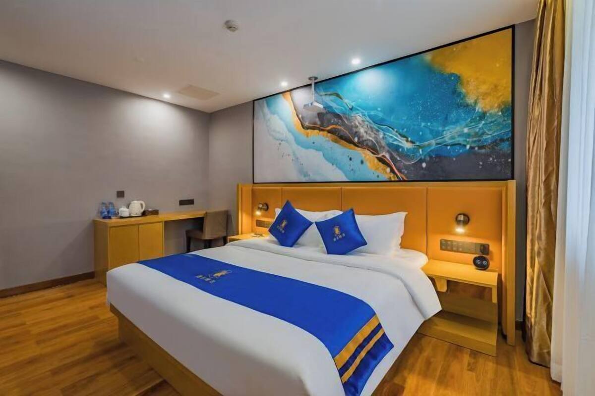A hotel room with a bed, bedside tables, a desk, a chair, a painting on the wall, and a curtain.