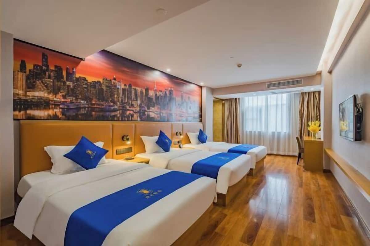 A hotel room with three beds, a cityscape painting, a television, and a window with curtains.