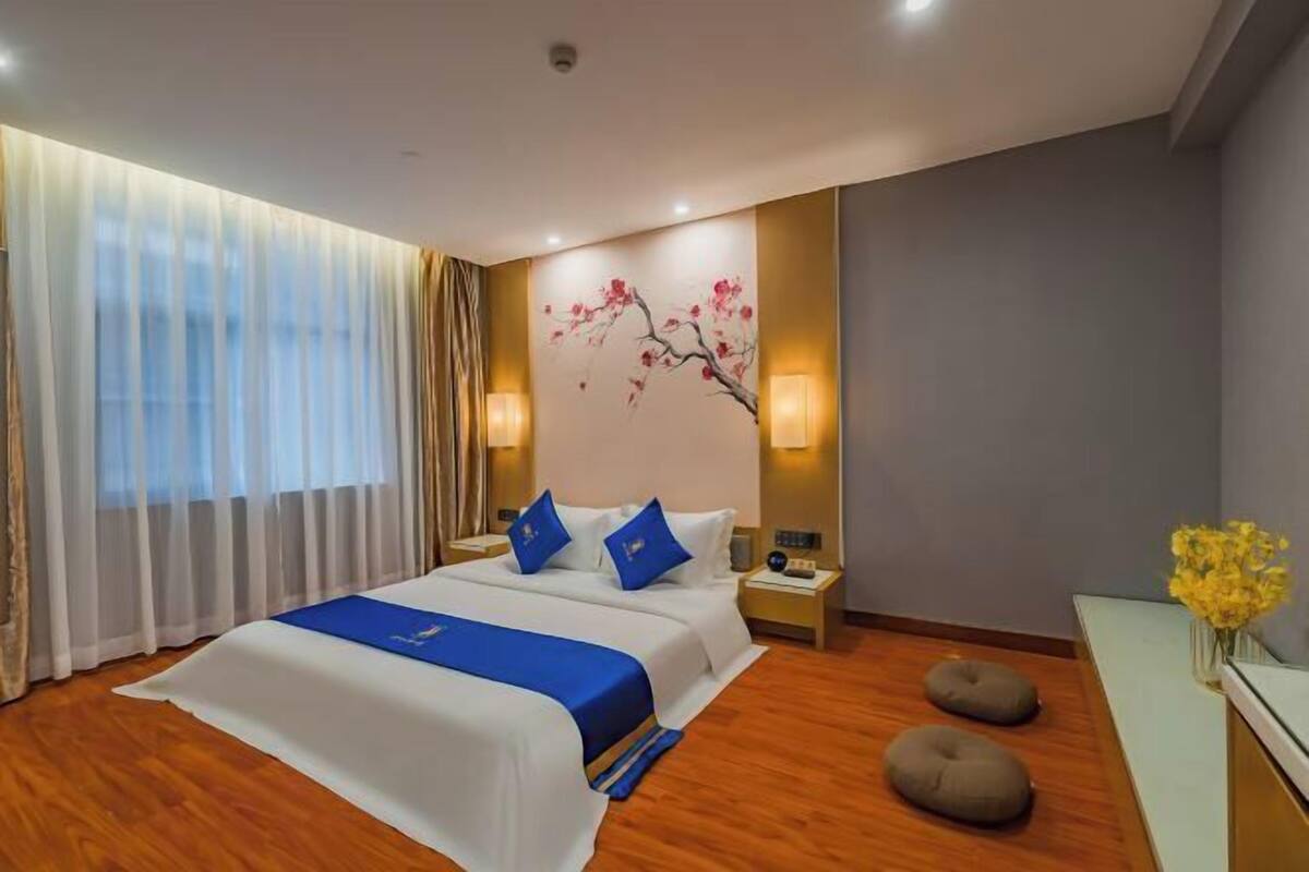 A hotel room with a large bed, two bedside tables, a wall-mounted lamp, and a decorative wall piece.