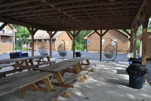Een overdekte picknickplaats met houten banken en hangstoelen, omringd door blokhutten.