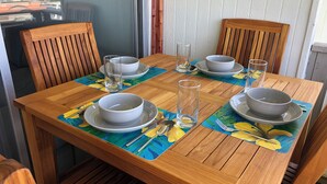 Une table à manger en bois, accompagnée de quatre chaises, mise avec des bols blancs, des assiettes et des verres transparents.