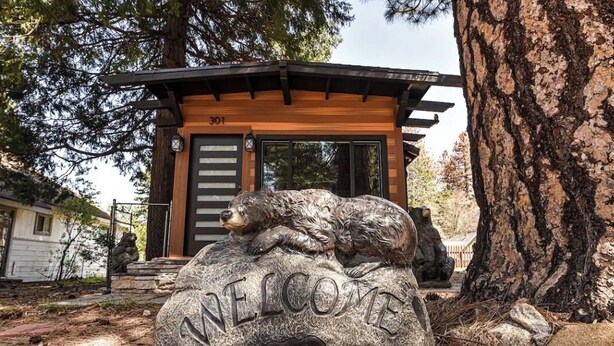 Une pancarte d’accueil représentant un ours et un chien, un bâtiment en bois avec le numéro de garage 301, et un grand arbre.