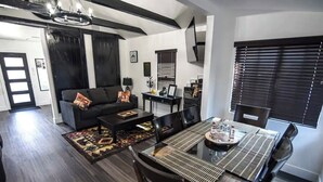 Un salon moderne avec un canapé noir, une table basse et une table à manger pour quatre personnes.