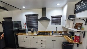 Une cuisine moderne avec des armoires blanches, une cuisinière noire et un réfrigérateur noir. On y trouve deux fenêtres équipées de stores, une hotte noire et une étagère où sont rangés des ustensiles de cuisine.