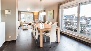 A modern dining area with a large table and chairs, a phone on the wall, and large windows offering a view of the city. - Maeterlinck 201 Sunny Penthouse in Koksijde (Koksijde)