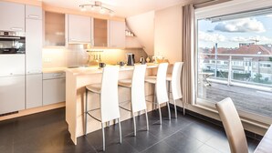 A modern kitchen with a central island, white bar stools, and a large window offering a city view. - Maeterlinck 201 Sunny Penthouse in Koksijde (Koksijde)
