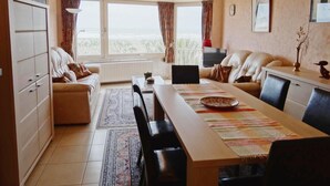 Una sala de estar amplia con un gran ventanal, un comedor con una mesa larga y un conjunto de sofás.