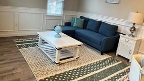 A living room with a blue sofa, a white coffee table, a patterned rug, and a small side table with a lamp. - 2 Bedroom Rental in Newport w/ Parking! Steps away from Thames, Broadway, & DT! (Newport)
