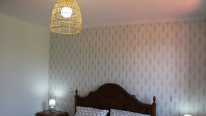 Camera da letto con testiera in legno, biancheria a motivi decorativi, due comodini con lampade e carta da parati strutturata.