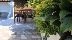 Una zona patio con pavimento in pietra, un tavolo di legno con sedie e diverse piante, tra cui una pianta con una grande foglia verde.