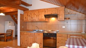 A cozy kitchen with wooden cabinets, a built-in oven, and a sink. There is a plaid chair and a table with a checkered tablecloth. - Belvilla by OYO Negritella Quadri Sette (Cavalese)