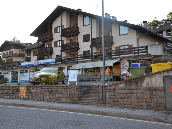 Un edificio de varios pisos con una planta baja que alberga una tienda Coop y una escalera visible que lleva a los pisos superiores.