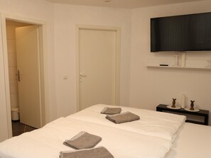 Una habitación de hotel con una cama, un televisor montado en la pared y una mesita de noche con lámpara.