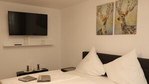 A neatly made bed with white and gray linens, a flat-screen TV mounted on the wall, and two paintings of deer on the wall. - Apartment With Terrace, Essen (Essen)