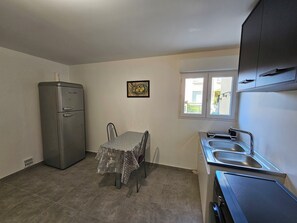A compact kitchen with a refrigerator, a dining table with chairs, a window with a view, and a sink. - Belle Maison Avec Jardin et Parking Gratuit -10% Séjour 7 j (Carcassonne)