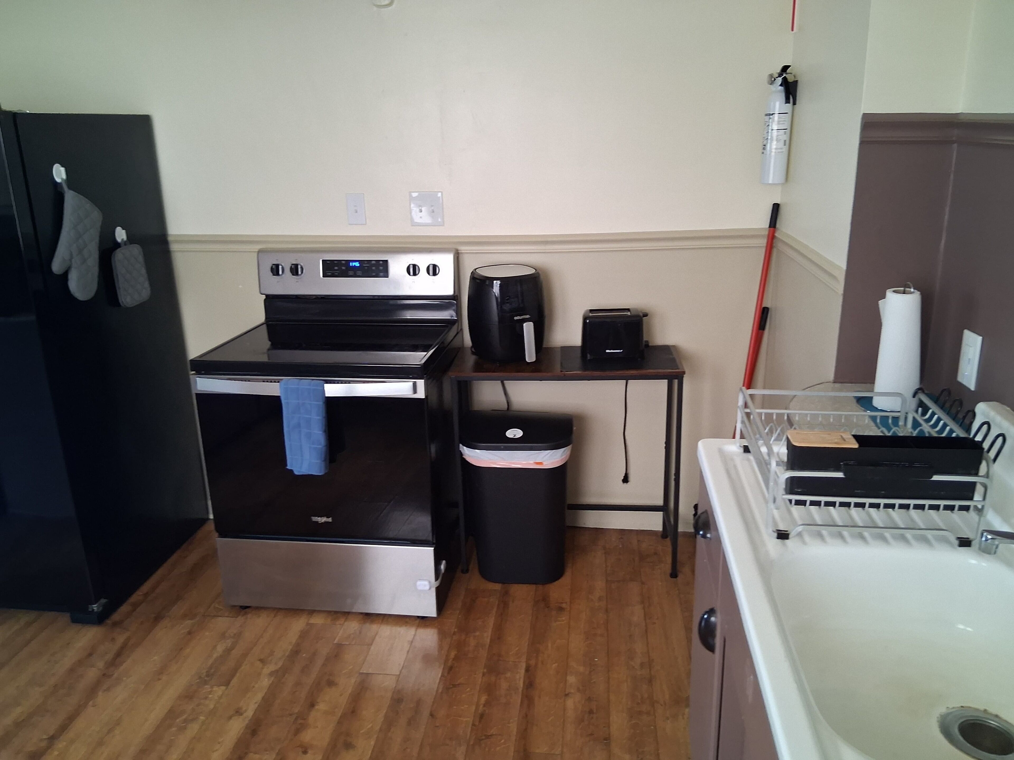 Uma cozinha compacta com forno de aço inoxidável, máquina de café, torradeira, lixeira e pia.