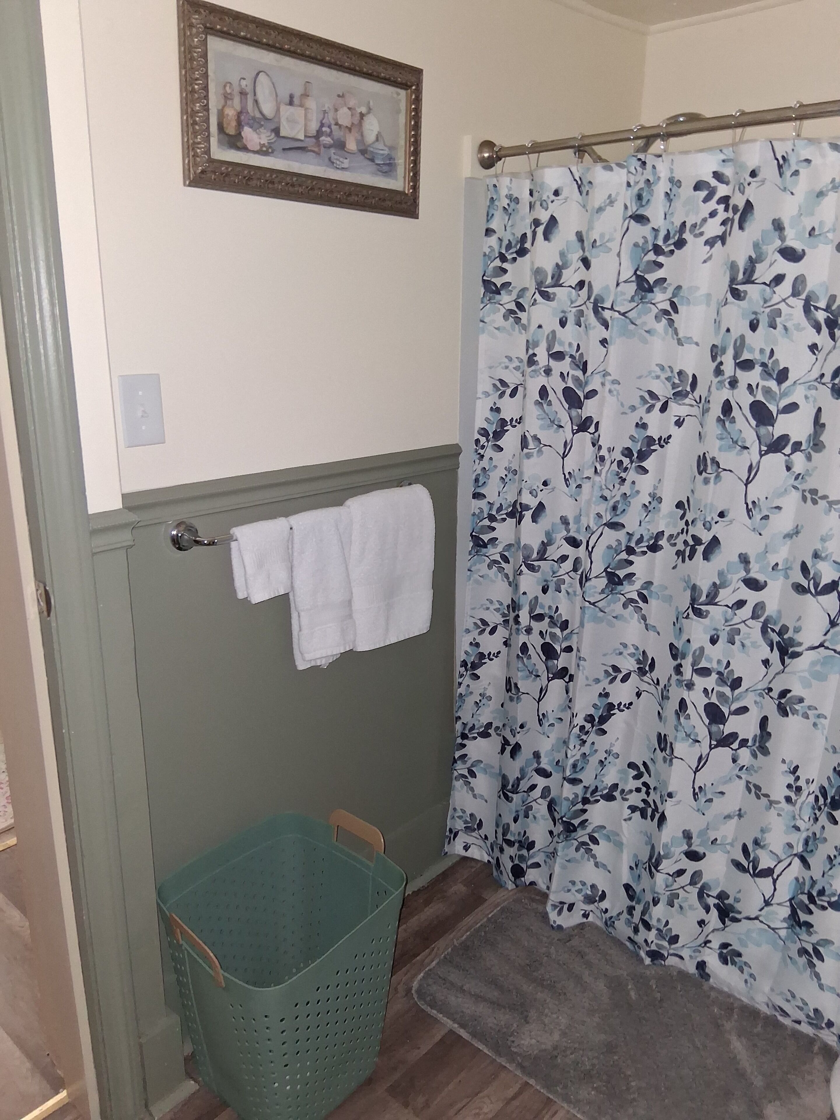 A bathroom with a shower curtain, a green basket, and a towel rack.