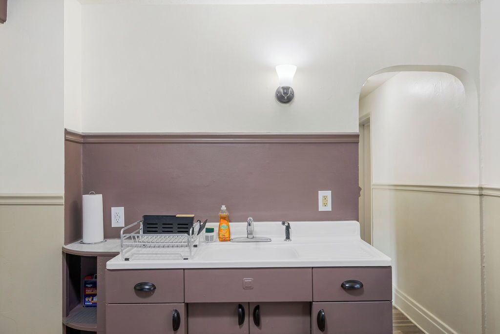 Une salle de bain avec un lavabo blanc, un miroir, un distributeur de serviettes et un distributeur de savon. On y trouve une étagère avec un porte-brosse à dents et une boîte de mouchoirs.
