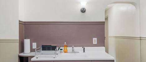 Une salle de bain avec un lavabo blanc, un miroir, un distributeur de serviettes et un distributeur de savon. On y trouve une étagère avec un porte-brosse à dents et une boîte de mouchoirs.