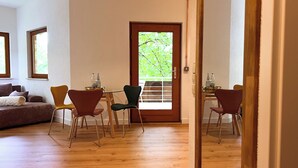 Una stanza con pavimento in legno, un divano, due poltrone, un tavolo con bottiglie e una porta che dà sull'esterno.