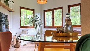 Zona pranzo moderna con tavolo in vetro, sedie di legno e lampadario.