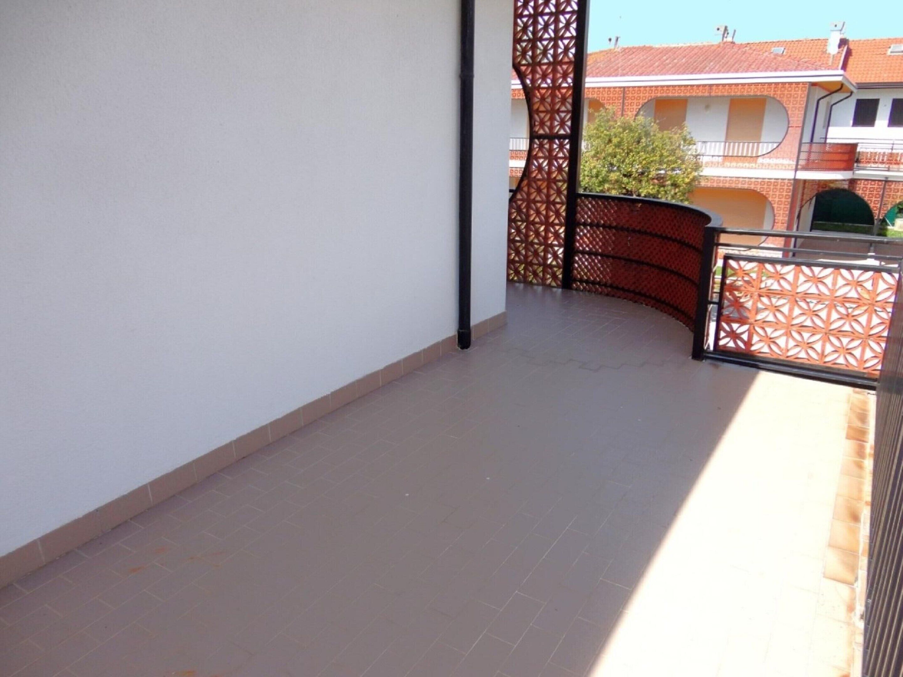A balcony with a tiled floor, a metal railing, and a view of a building with red-tiled roofs.