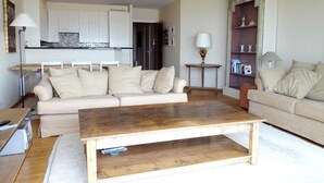 A living room with a wooden coffee table, two beige sofas, a small side table with a lamp, and a bookshelf. - Seaside Comfort With Parking (Nieuwpoort)