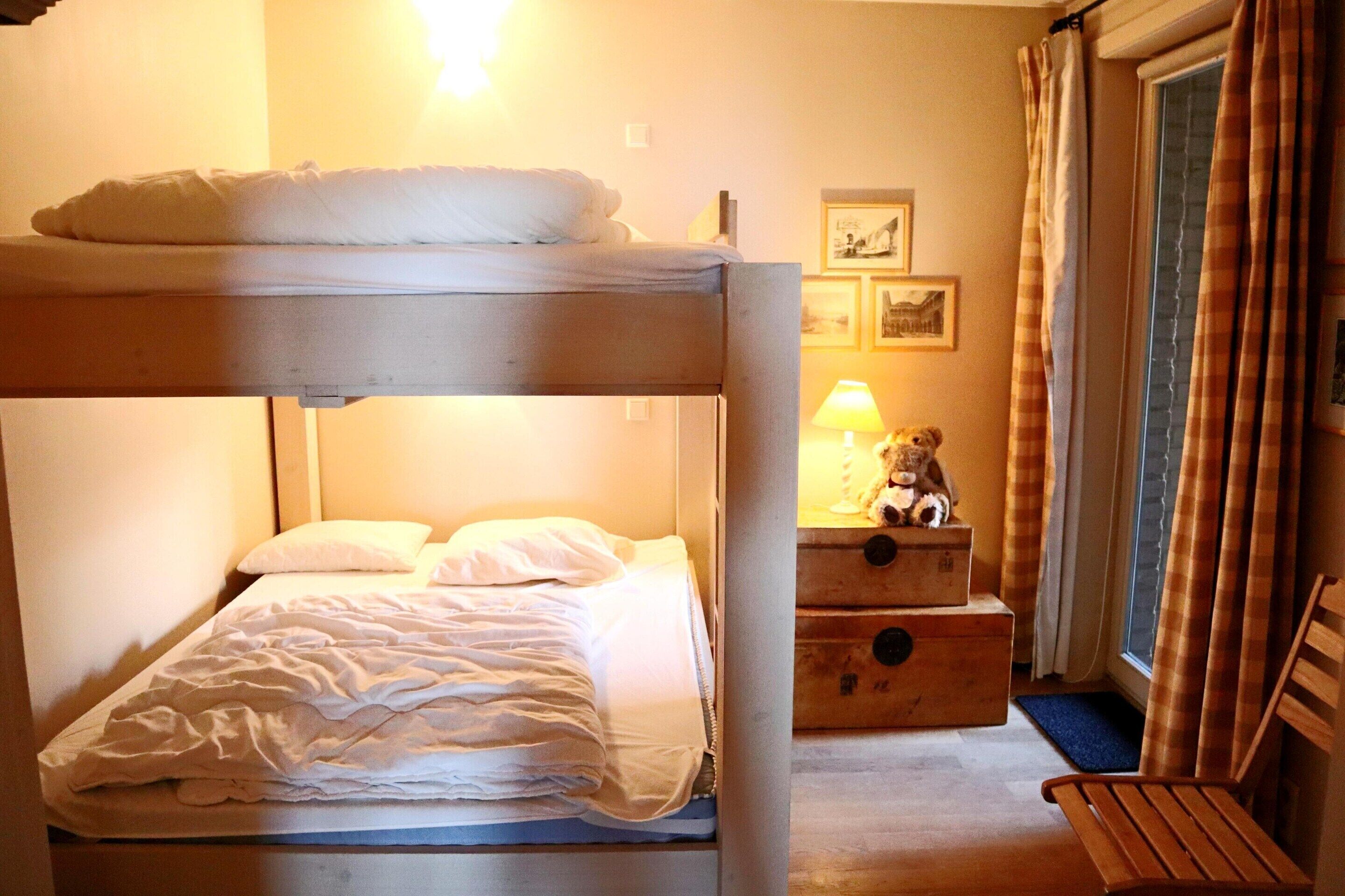 A bunk bed with a wooden headboard, a bedside table with a lamp, and a teddy bear on the nightstand.