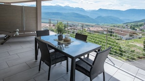Een balkon met een tafel en stoelen, uitkijkend op een bergachtig landschap.