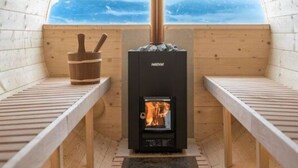 Een houten sauna met een open haard, banken en uitzicht op de bergen.