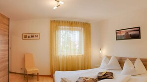 Een hotelkamer met een bed, een stoel, een raam met gordijnen, een aan de muur hangend schilderij en een plafondlamp.