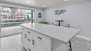 A modern kitchen with a large island, white cabinetry, and a view of a pool area. - HEATED POOL screened in - PET - TIKI - 4 Kayaks - Private Fishing & Boating Dock (Hernando Beach)