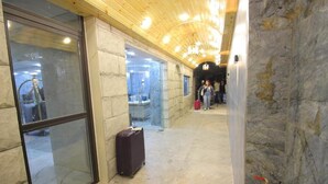 A hallway with stone walls, a wooden ceiling, and a glass door leading to a room with a bathtub. - Beirut Hotel Two (Amman)