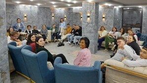 A group of people seated in a modern, well-lit room with marble walls and blue chairs. - Beirut Hotel Two (Amman)
