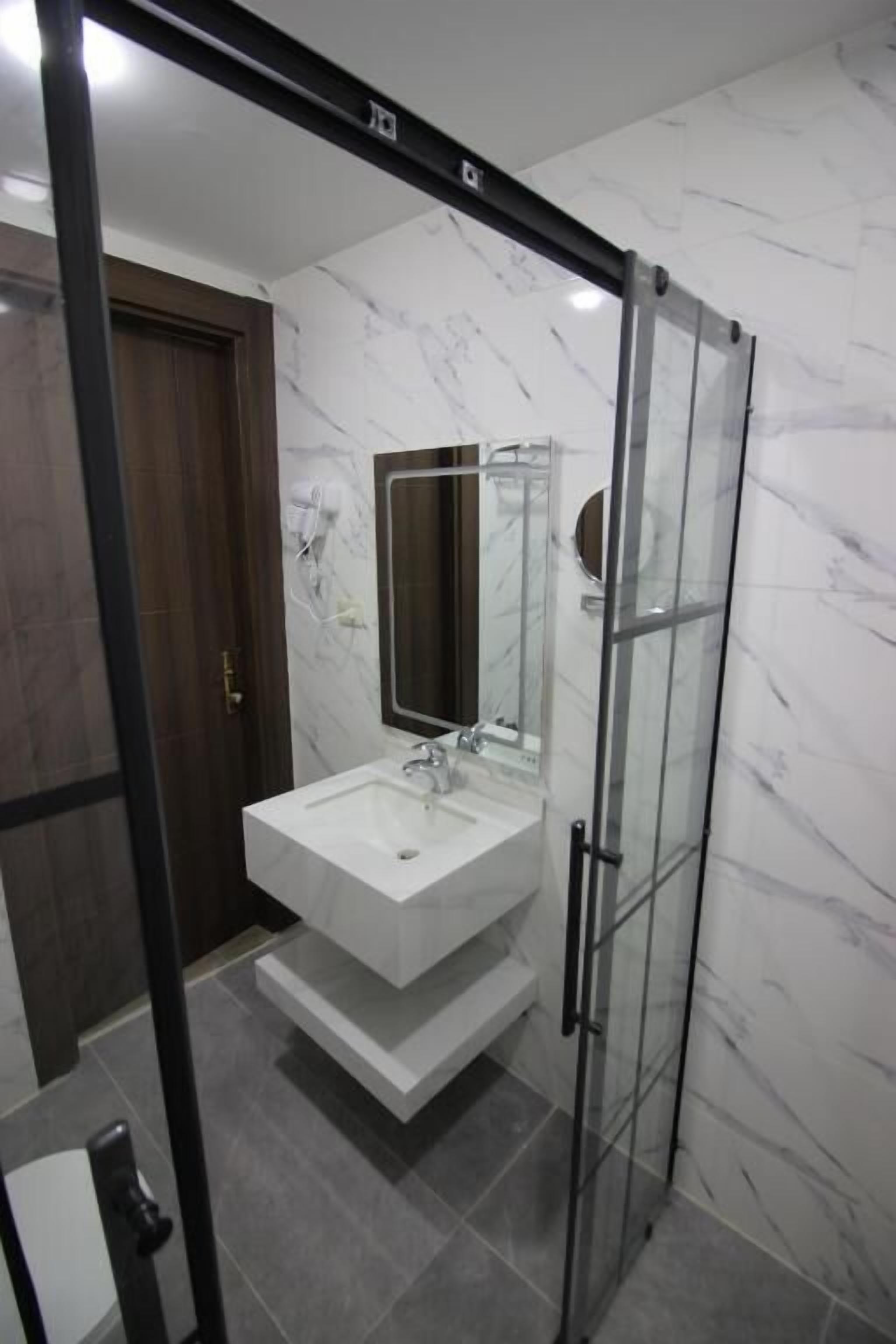 A modern bathroom with a glass shower enclosure, a white sink, and a marble wall.