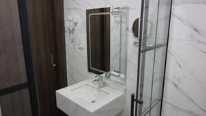 A modern bathroom with a glass shower enclosure, a white sink, and a marble wall. - Beirut Hotel Two (Amman)