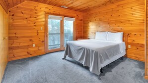 A bedroom with wooden walls, a bed with white linens, a ceiling fan, and a large window.