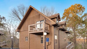 A wooden cabin with a balcony, a covered porch, and a small deck.