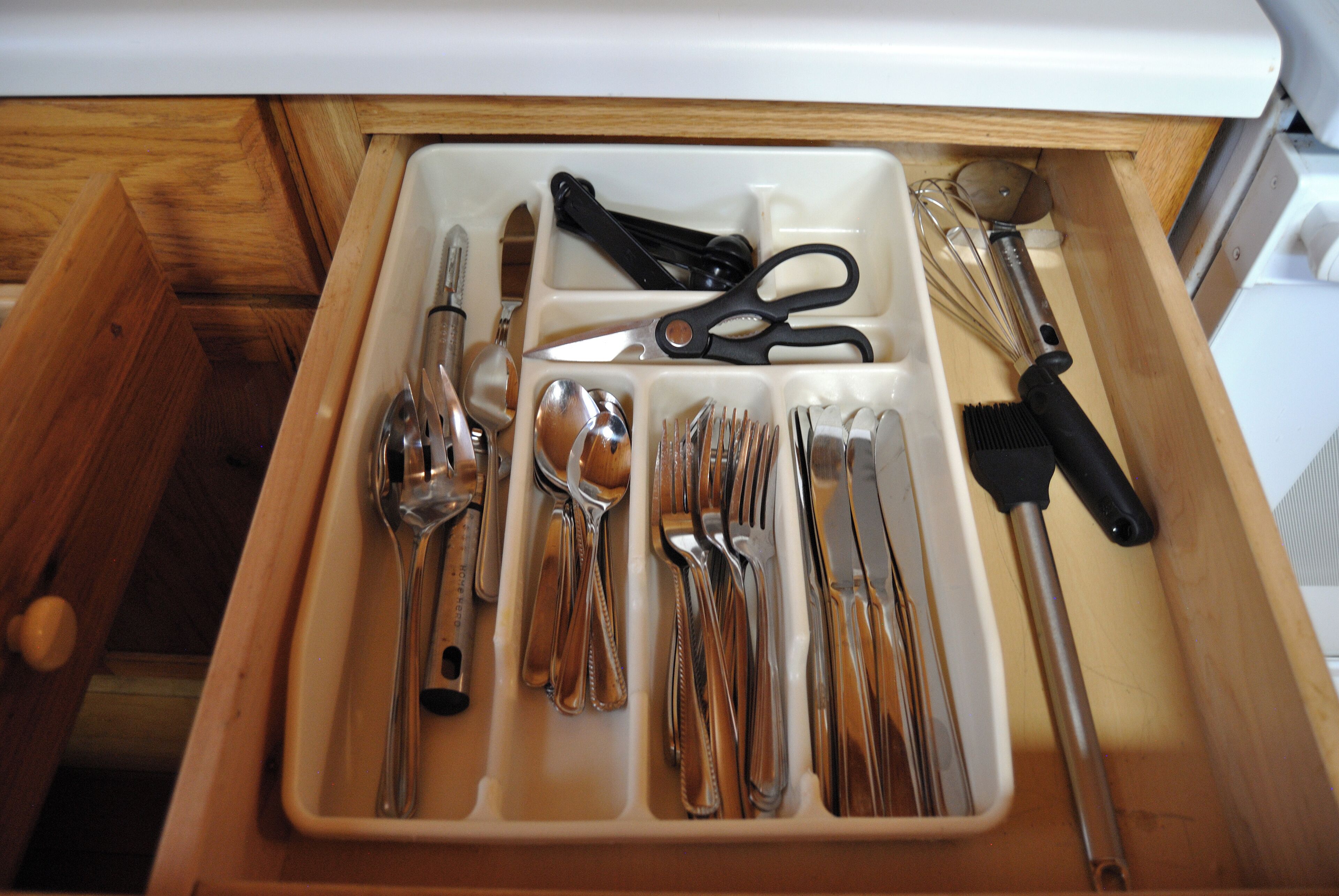 Un cajón con utensilios de cocina ordenados, incluyendo cucharas, tenedores, cuchillos y un batidor.