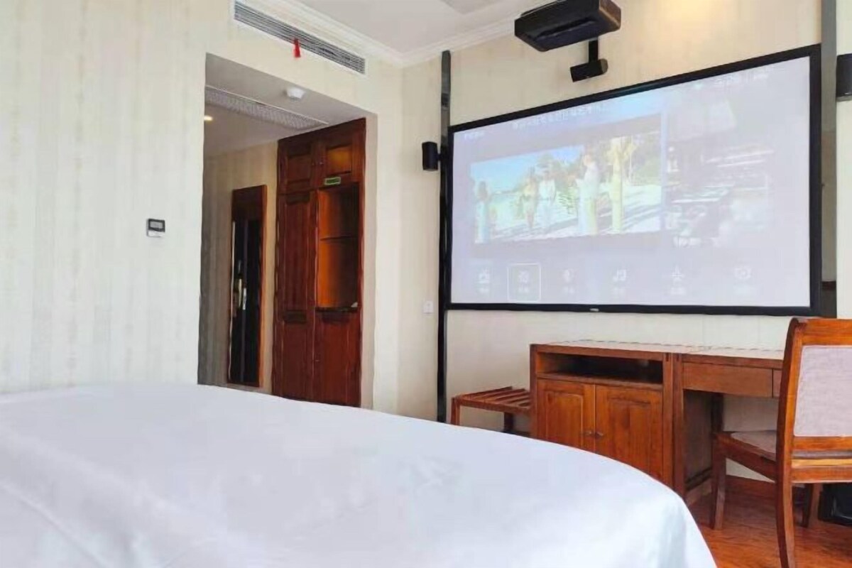 A hotel room with a bed, a desk, a chair, and a projector screen displaying a presentation.