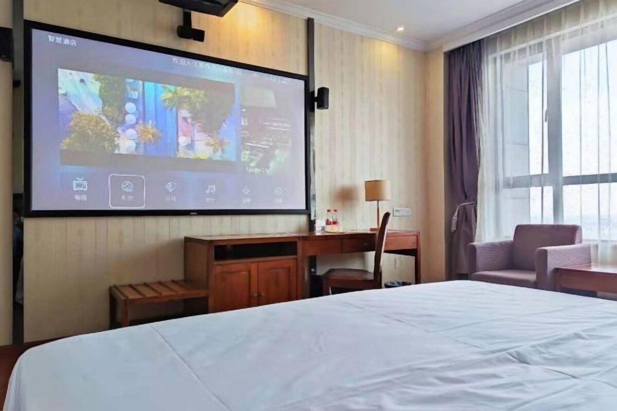 A hotel room with a bed, a desk, a chair, a TV screen, and a window with curtains.