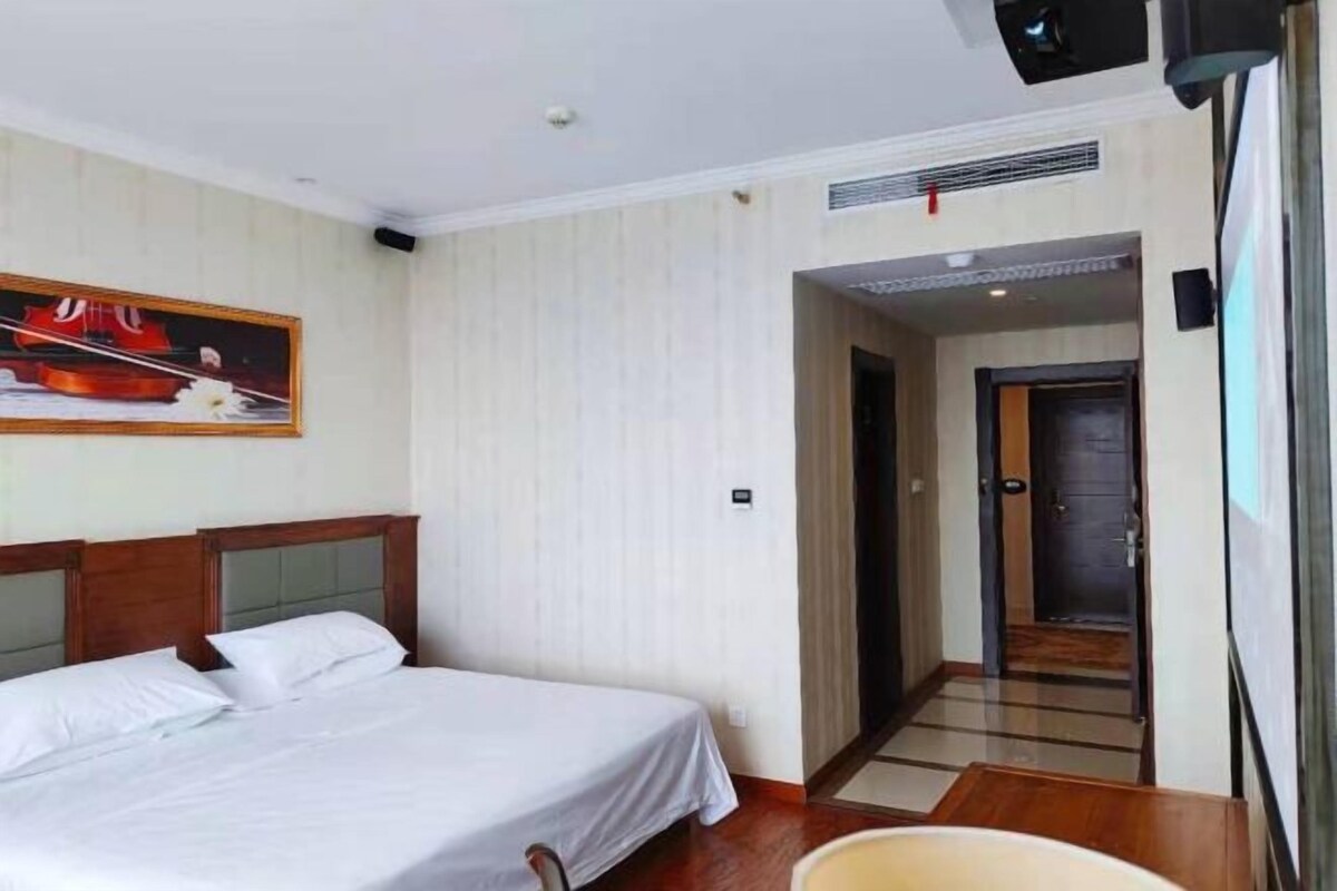 A hotel room with a bed, a painting on the wall, a door, and a hallway.